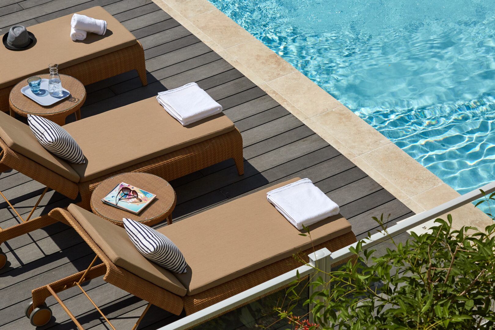 Chaises longues en rotin au bord de la piscine avec coussins rayés et tables d'appoint.